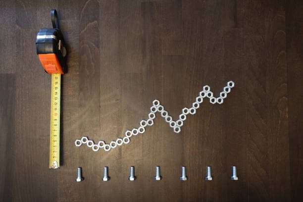 Steel nuts and bolts arranged as a rising chart with a tape measure